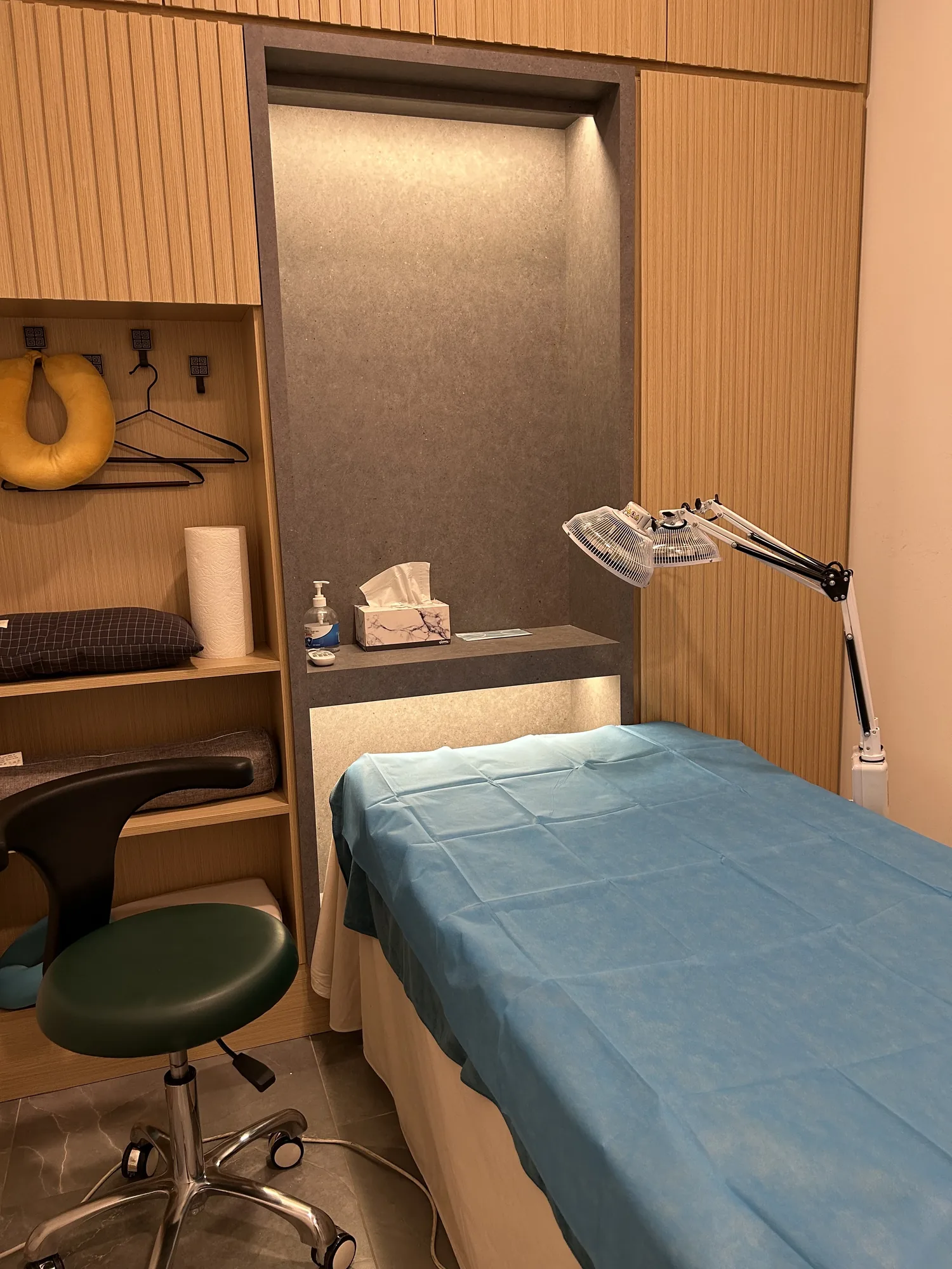 Treatment room with blue-sheeted bed, TDP heat lamp and green stool at Prime and Naturals